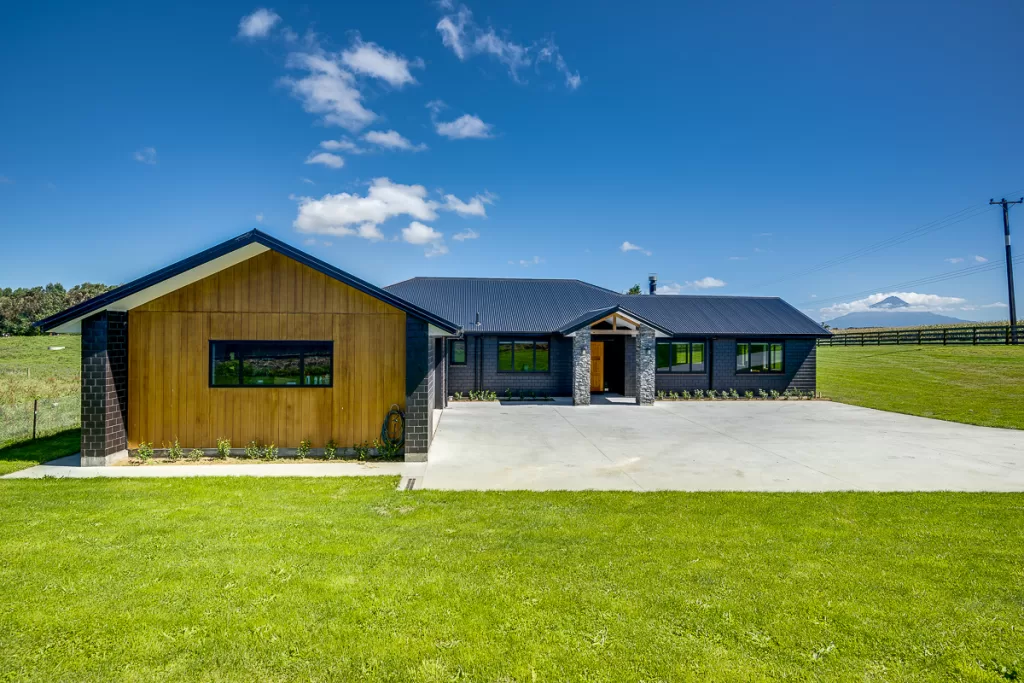 Ohangai Rd project proudly designed and built by BuildtechNZ - Bespoke New Home Builders. Exterior shot showing cedar cladding, exposed trusses, stone work. 